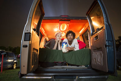 Couple holding popcorn while sitting in camping van during drive-in movie