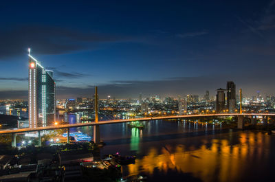 Illuminated buildings by river against sky in city at night