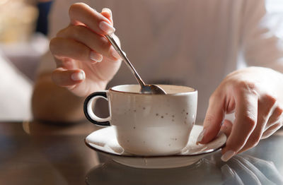 Closeup of female hands with french manicure holding cozy ceramic white mug of tea or coffee