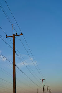 Low angle view of electricity pylon against clear blue sky