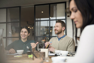 Happy business people talking while having coffee at table during meeting in office