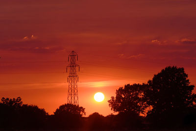 Silhouette trees and electricity pylon against romantic sky at sunset