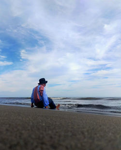 Man sitting at beach against sky