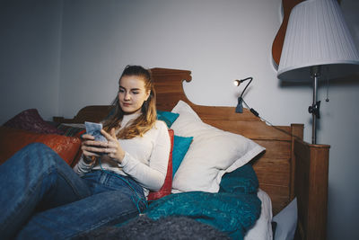 Young woman sitting on bed using mobile phone at dorm room