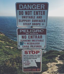 Close-up of warning sign by sea against sky