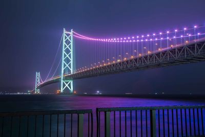 Illuminated bridge over river against sky at night