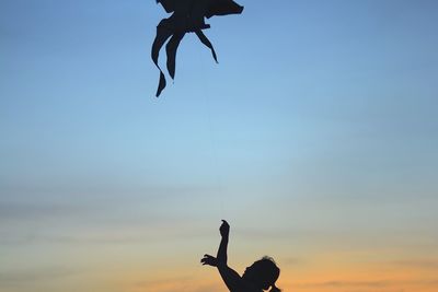 Close-up of silhouette woman flying kite against sky during sunset