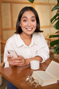 Portrait of young woman using mobile phone while sitting on table