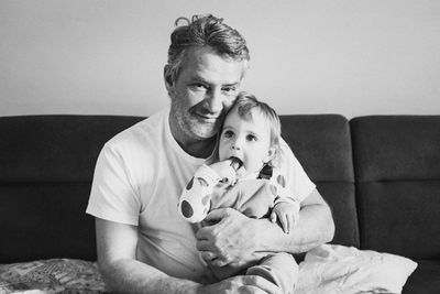 Portrait of smiling man sitting with toddler son on sofa at home