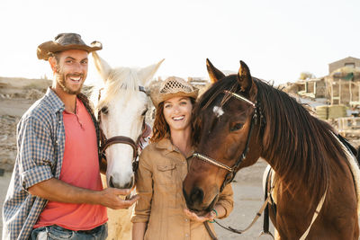 Portrait of cheerful couple standing by horse against clear sky