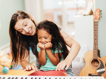 Happy mother teaching piano to daughter at home