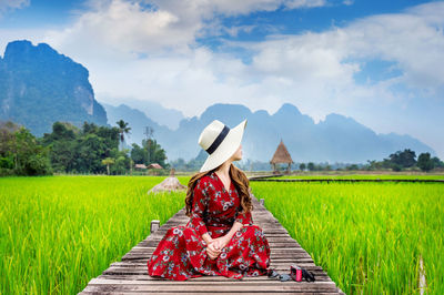 Mid adult woman sitting on boardwalk against cloudy sky