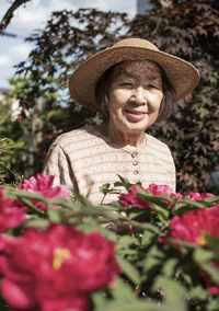 Portrait of senior woman wearing hat standing amidst flowering plants