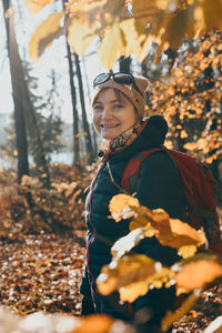 Woman with backpack wandering in a forest on autumn sunny day. front view of middle age active woman