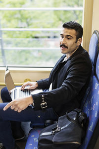 Side view of young man pointing while using laptop in tram