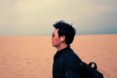 Side view of man listening to music while standing at sandy beach