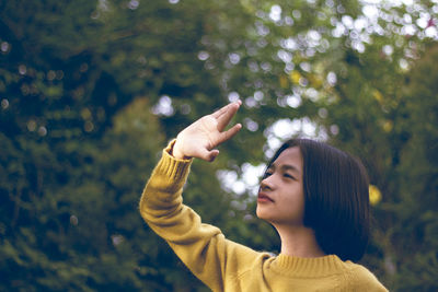 Cute girl shielding eyes while standing against trees