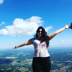 Young woman with arms raised standing against sky