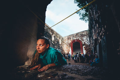 Man looking away while sitting on historic building against sky