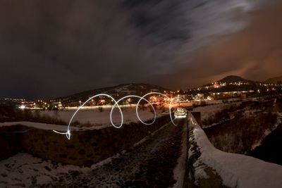 Illuminated city by road against sky at night