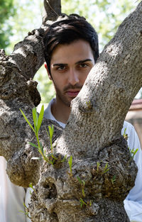 Portrait of young man against tree trunk