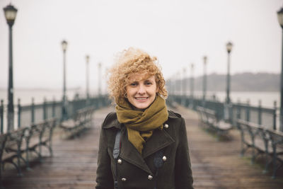 Portrait of young woman standing on pier against sky during foggy weather