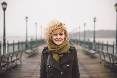 Portrait of young woman standing on pier against sky during foggy weather