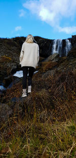 Rear view of woman walking on mountain against waterfall