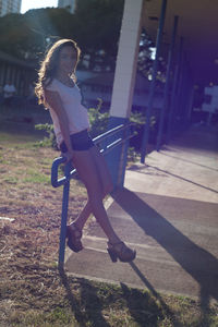 Full length of young woman sitting on metallic railing during sunny day