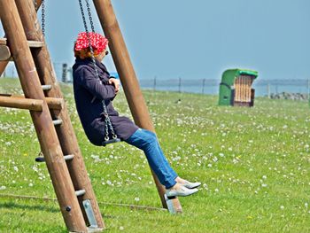 Side view of woman sitting swing over grassy land
