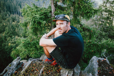 Side view portrait of man sitting on rocks in forest