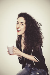 Portrait of smiling young woman sitting against gray background