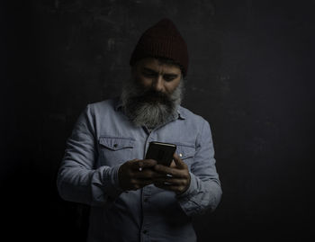  man with beard and mustache chatting with cellphone. jeans shirt, wool hat and mobile in hand.