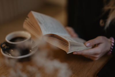 Close-up of woman holding coffee cup on table