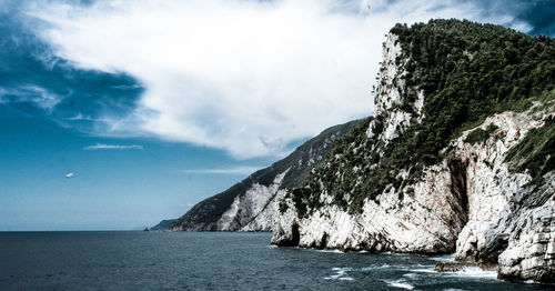 Scenic view of sea by mountain against sky