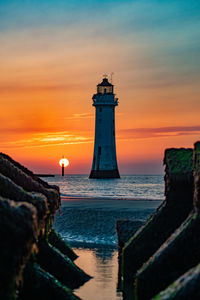 Lighthouse by sea against sky during sunset