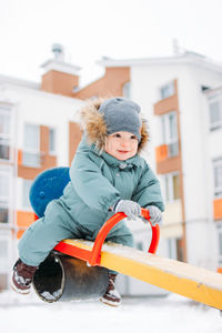 Cute baby boy sitting on seesaw during winter