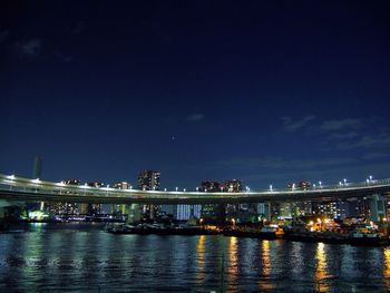 Illuminated bridge over river against sky at night