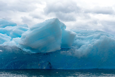 Icebergs in sea against cloudy sky