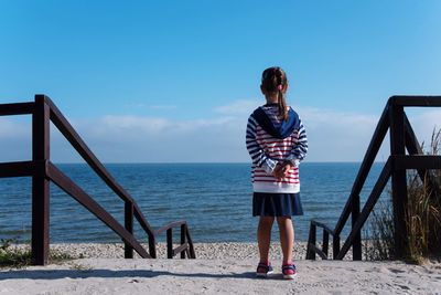 Rear view of girl standing on steps against sea