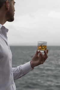 Man holding glass of whiskey by sea