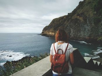 Rear view of woman standing on cliff by sea