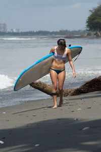 Full length of young woman holding surfboard walking at beach