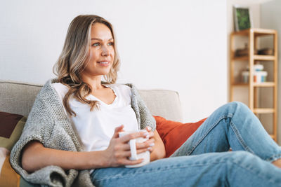 Young beautiful woman forty year with blonde long curly hair in cozy knitted grey sweater at home