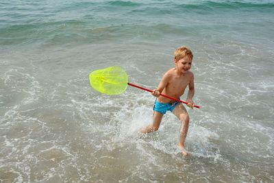 High angle view of boy holding fishing net running on shore at beach