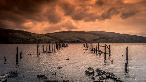 Wooden posts in lake against sky