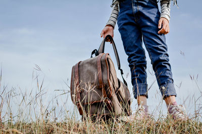 Low section of girl with backpack standing on field against sky