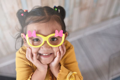 High angle view of a smiling little asian girl wearing fancy glasses.