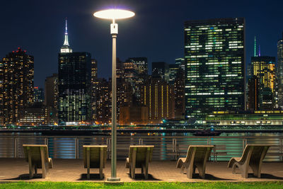 Empty chairs against illuminated empire state building in city at night