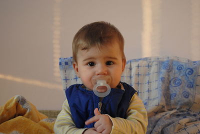 Portrait of cute baby boy with pacifier in mouth sitting at home